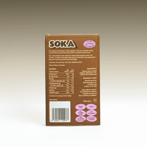The back of a SOKA coffee concentrate box, showing product details, nutrition facts, ingredients, and barcodes of the hazelnut flavour, photographed against a neutral grey/brown gradient backdrop.