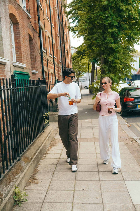A young man and woman walking on a city sidewalk, each holding a coffee cup made with SOKA espresso concentrate.