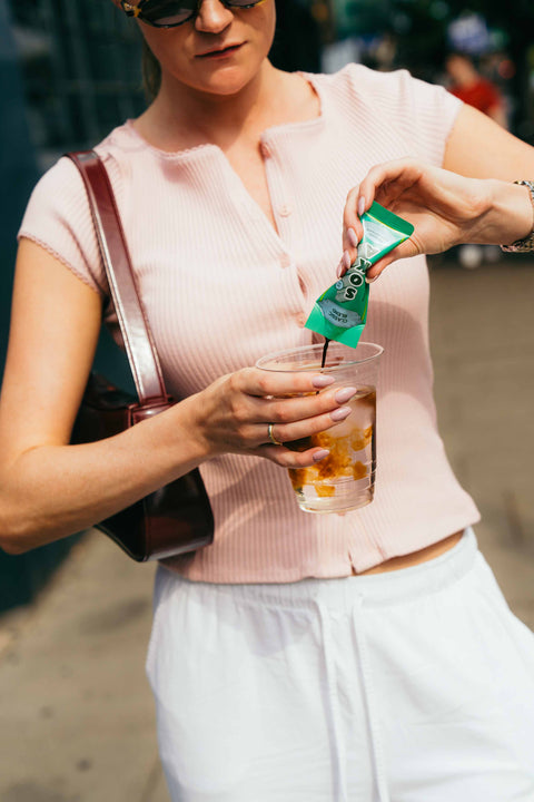 A young woman on the go pours coffee from a sachet into a cup of water.